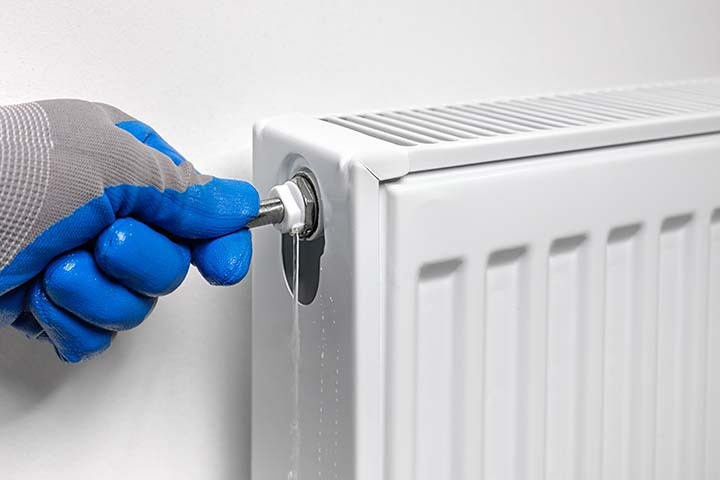 Person bleeding a radiator using a bleed key near valve